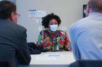 A seated woman wearing a colorful blouse gestures as she speaks